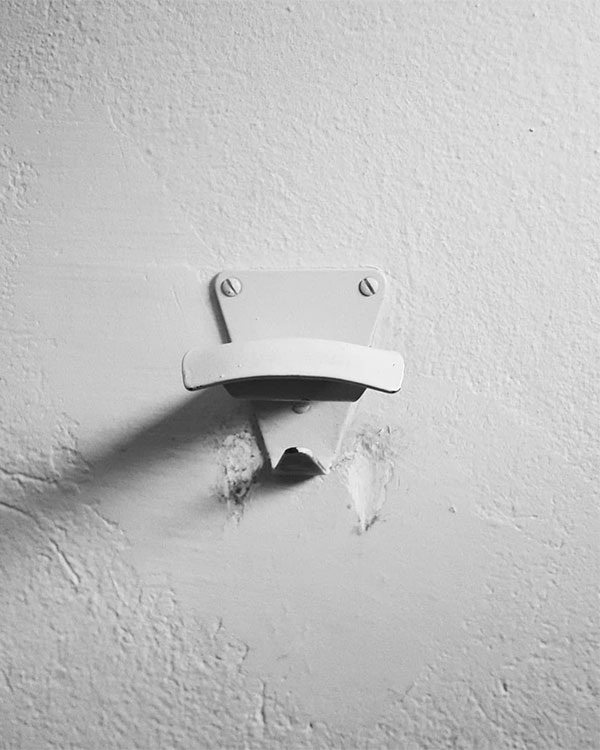 A double hook made of metal, gray paint, screwed to a wall. Found on a Sport Club in Apt, France, 2018.