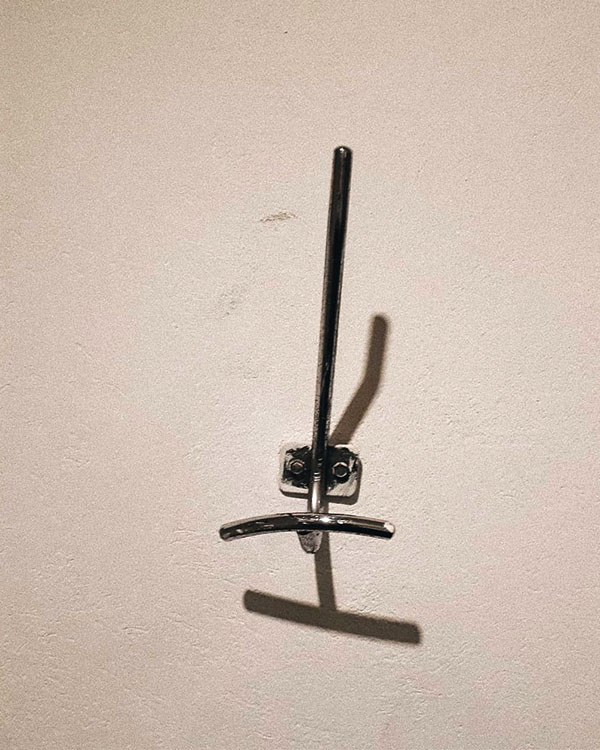 A double hook made of metal, chrome, screwed to a wall. Found on a private home in Mexico City, Mexico, 2020.