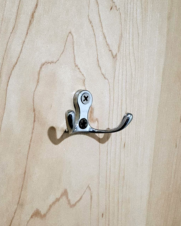 A double hook made of metal, chrome, screwed to a door. Found on a restaurant in Mexico City, Mexico, 2019.