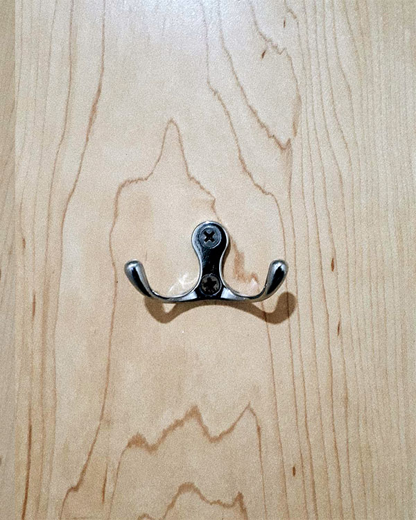 A double hook made of metal, chrome, screwed to a door. Found on a restaurant in Mexico City, Mexico, 2019.