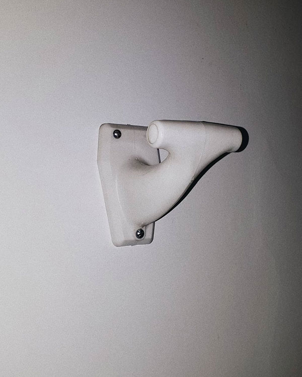 A single hook made of white plastic, screwed to a door. Found on a private home in Val-d'Isère, France, 2020.