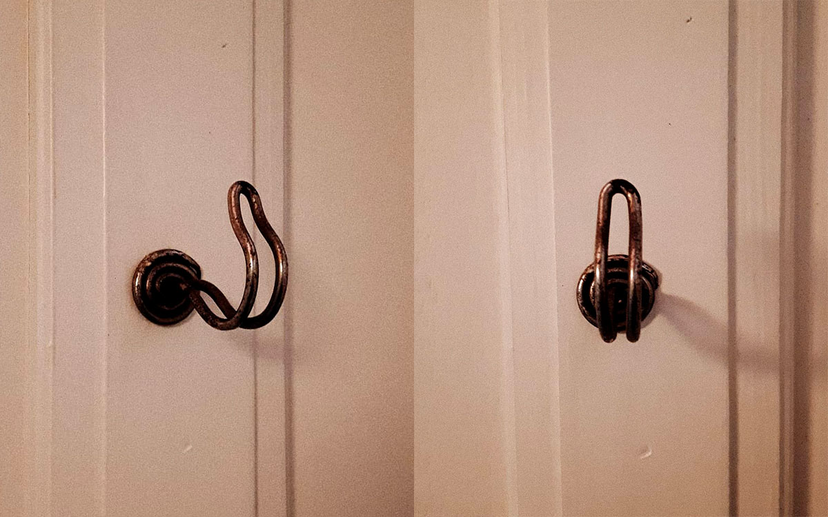 A single hook made of metal, nickel, screwed to a wall. Found on a private home in Apt, France, 2021.