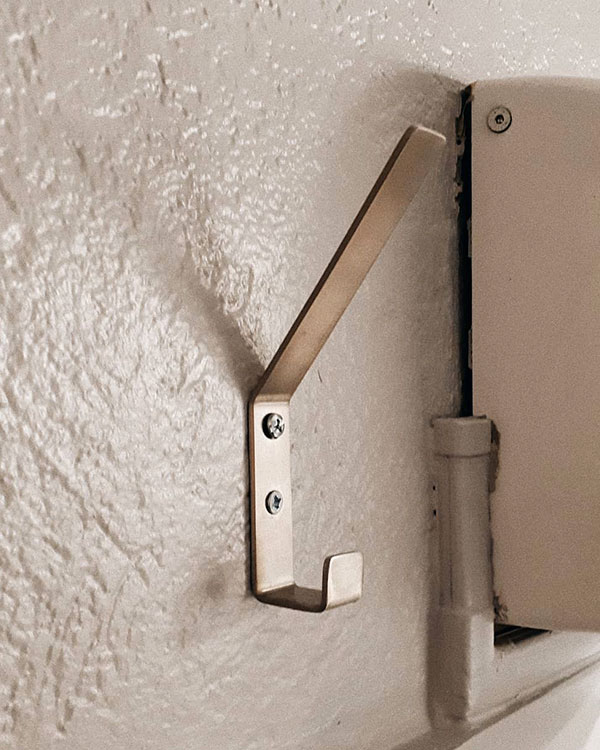 A double hook made of metal, nickel, screwed to a wall. Found on a restaurant in Lyon, France, 2021.