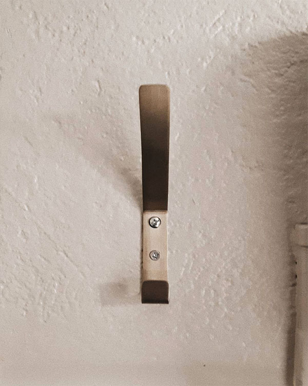 A double hook made of metal, nickel, screwed to a wall. Found on a restaurant in Lyon, France, 2021.