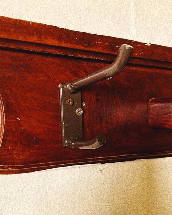 A double hook made of metal, brown paint, screwed to a piece of wood. Found at Baños Termales de Ojocaliente in Aguascalientes, Mexico, 2022.