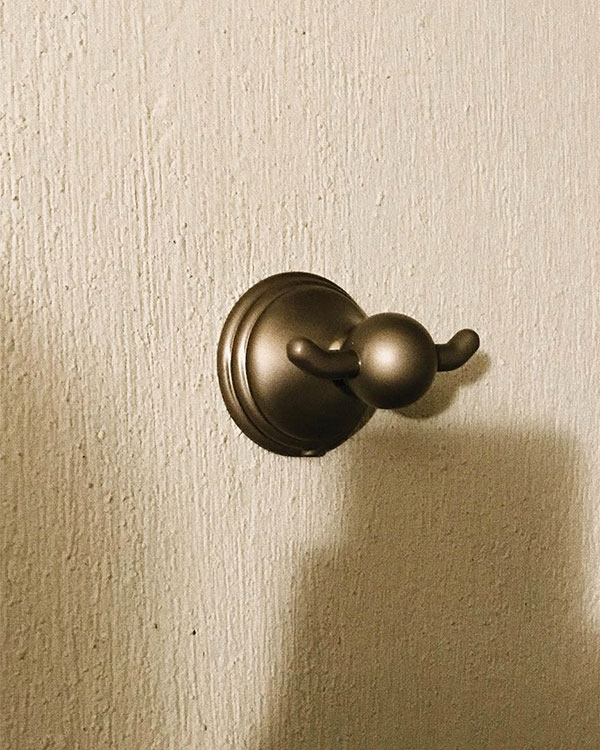 A double hook made of metal, brass, screwed to a wall. Found on a private home in Aguascalientes, Mexico, 2022.