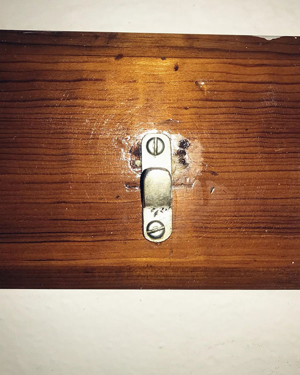 A single hook made of metal, brass, screwed to a piece of wood then to a wall. Found on a Sport Club in Mexico City, Mexico, 2022.