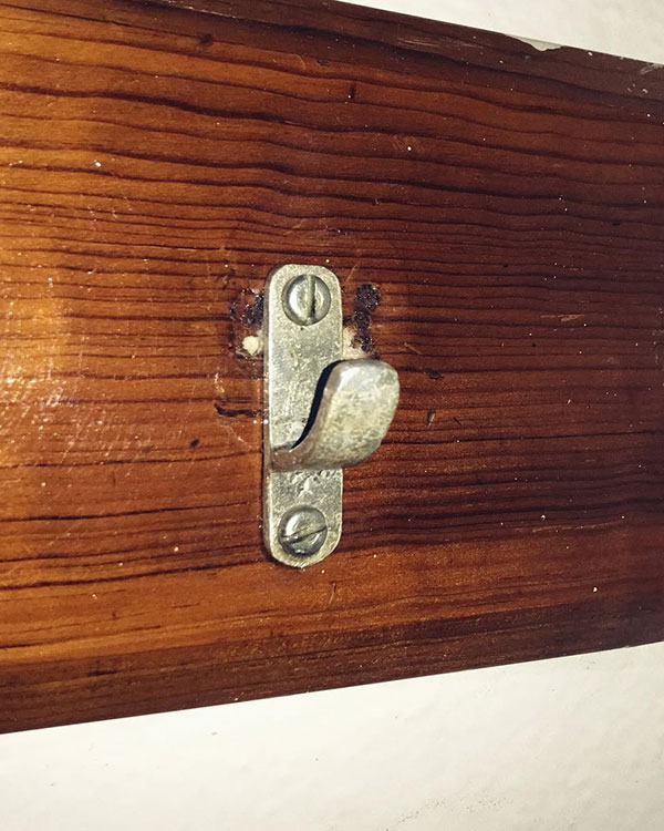 A single hook made of metal, brass, screwed to a piece of wood. Found at Club Mundet in Mexico City, Mexico, 2022.