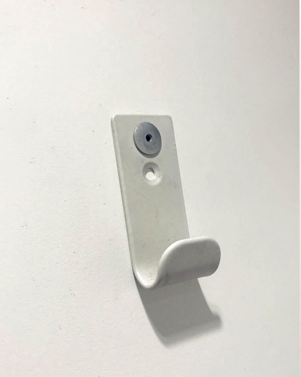 A single hook made of white plastic, riveted to a door. Found on a public bathroom in Avignon, France, 2022.