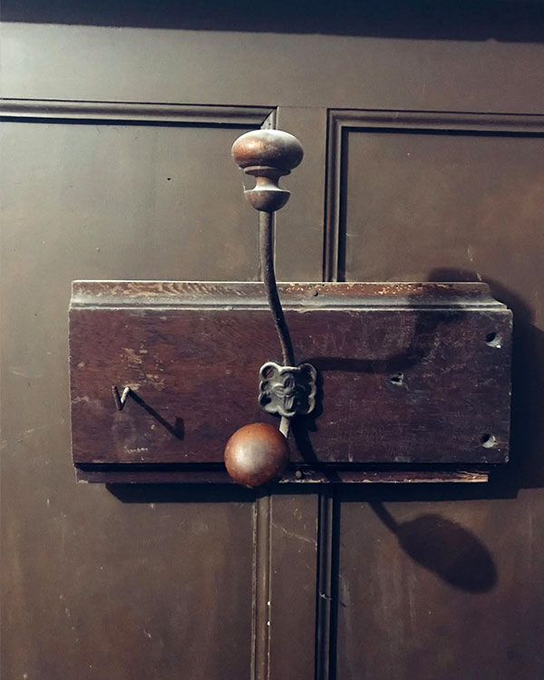 A double hook made of metal and wood, oxide, screwed to a piece of wood then to a door. Found on a private home in Apt, France, 2022.