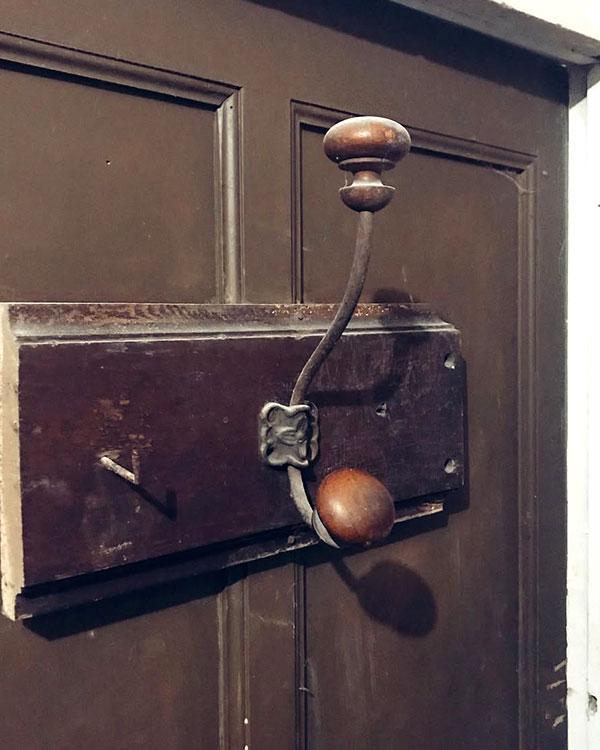 A double hook made of metal and wood, brass, screwed to a piece of wood. Found on a private home in Apt, France, 2022.