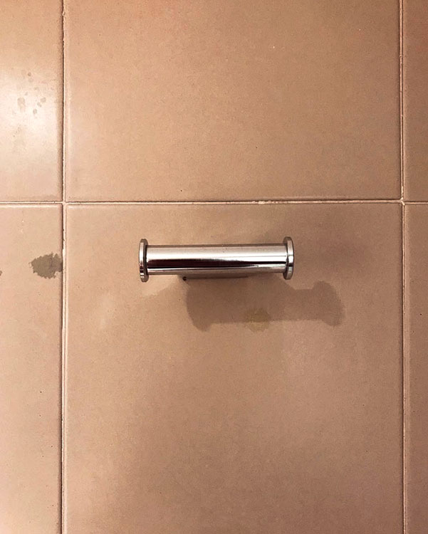 A double hook made of metal, chrome, fixed to a wall. Found on a hotel in Roses, Spain, 2022.