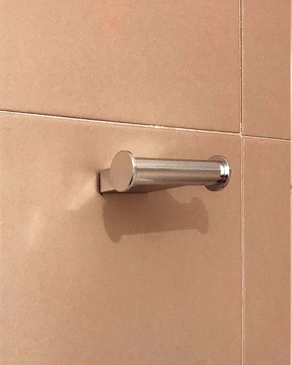 A double hook made of metal, chrome, screwed to a wall. Found on a hotel in Roses, Spain, 2022.