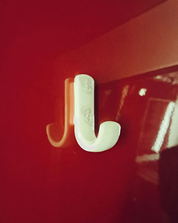 A single hook made of ivory plastic, screwed to a wall. Found on a train in Amsterdam, Netherlands, 2023.