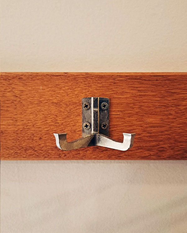 A double hook made of metal, nickel, screwed to a piece of wood then to a wall. Found on a museum in Brussels, Belgium, 2023.