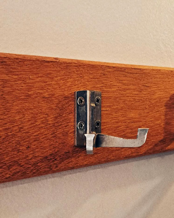 A double hook made of metal, nickel, screwed to a piece of wood. Found at Centre Belge de la Bande Dessinée in Brussels, Belgium, 2023.