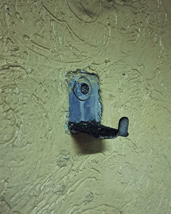 A single hook made of metal, gray paint, screwed to a wall. Found on a restaurant in Mexico City, Mexico, 2023.