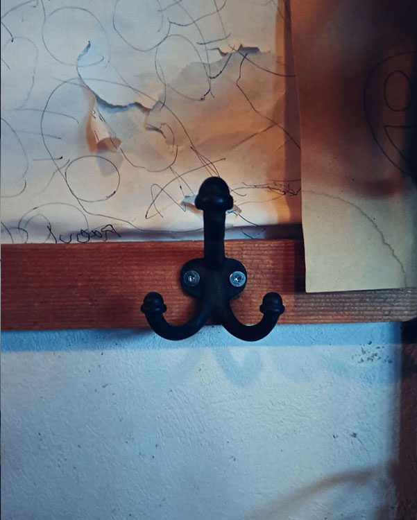 A triple hook made of metal, black paint, screwed to a wall. Found on a private home in Montreal, Canada, 2024.