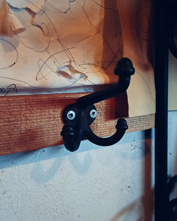 A triple hook made of metal, black paint, screwed to a wall. Found on a private home near Montreal, Canada, 2024.