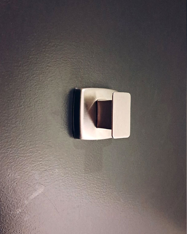 A single hook made of metal, nickel, screwed to a door. Found at Montreal Science Centre in Montreal, Canada, 2024.