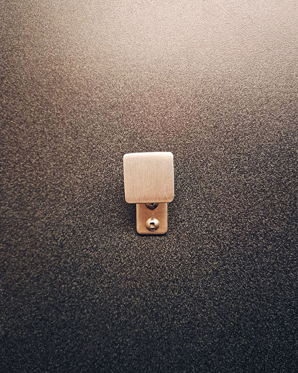 A single hook made of metal, nickel, riveted to a door. Found on an airport in Montreal, Canada, 2024.