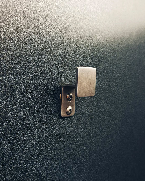 A single hook made of metal, nickel, riveted to a door. Found at Montréal–Trudeau International Airport, Montreal, Canada, 2024.