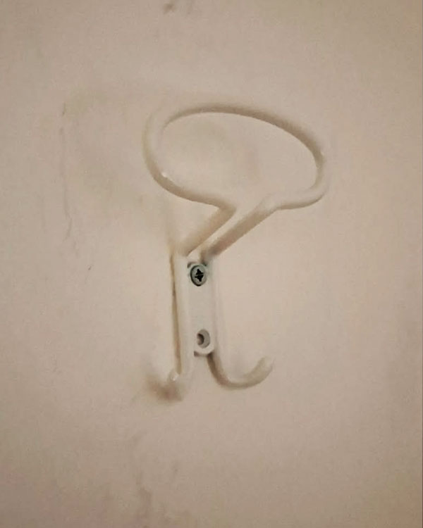 A triple hook made of metal, white powder coating, screwed to a wall. Found on a hotel in Pietra Ligure, Italy, 2024.
