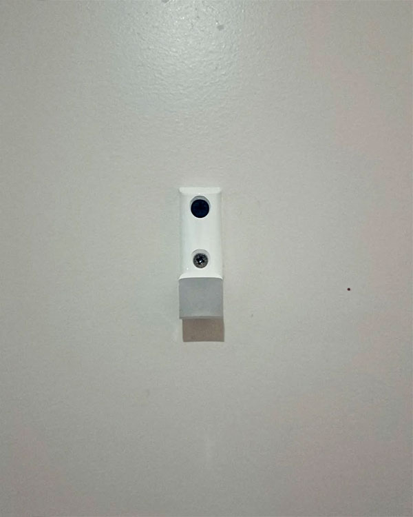 A single hook made of white plastic, screwed to a door. Found on a hotel in Lyon, France, 2024.