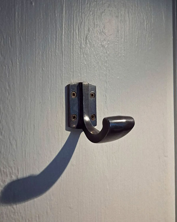A single hook made of metal, nickel, screwed to a door. Found on a restaurant in Paris, France, 2024.