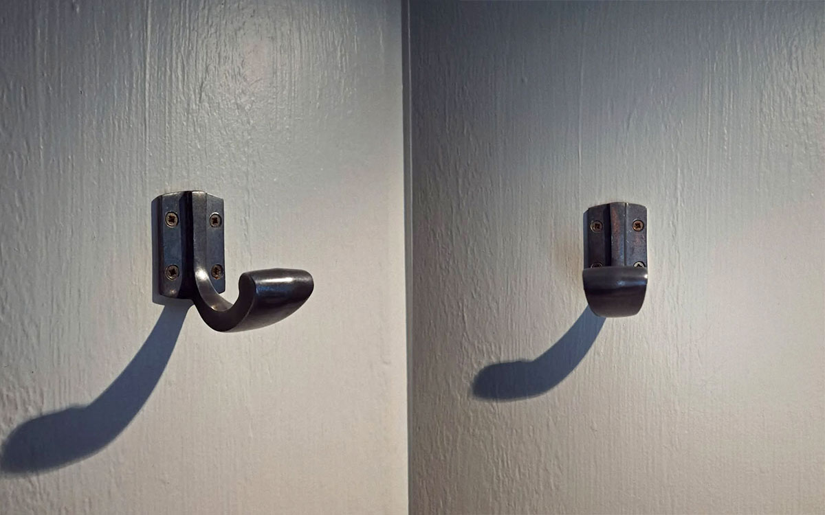 A single hook made of metal, nickel, screwed to a door. Found on a restaurant in Paris, France, 2024.