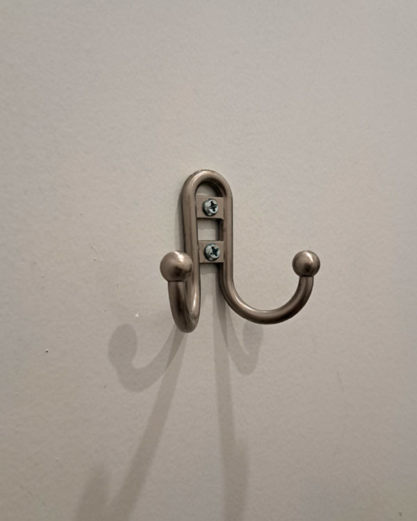 A double hook made of metal, nickel, screwed to a door. Found on a restaurant in NY, USA, 2025.