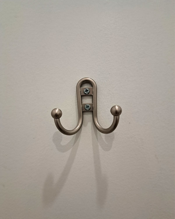 A double hook made of metal, nickel, screwed to a door. Found on a restaurant in NY, USA, 2025.