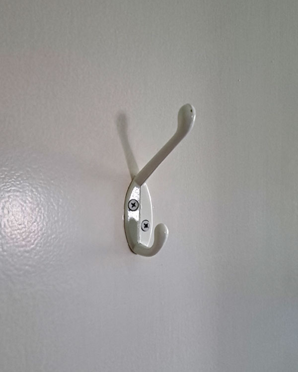 A double hook made of metal, white coating, screwed to a door. Found on a private home near NY, USA, 2025.