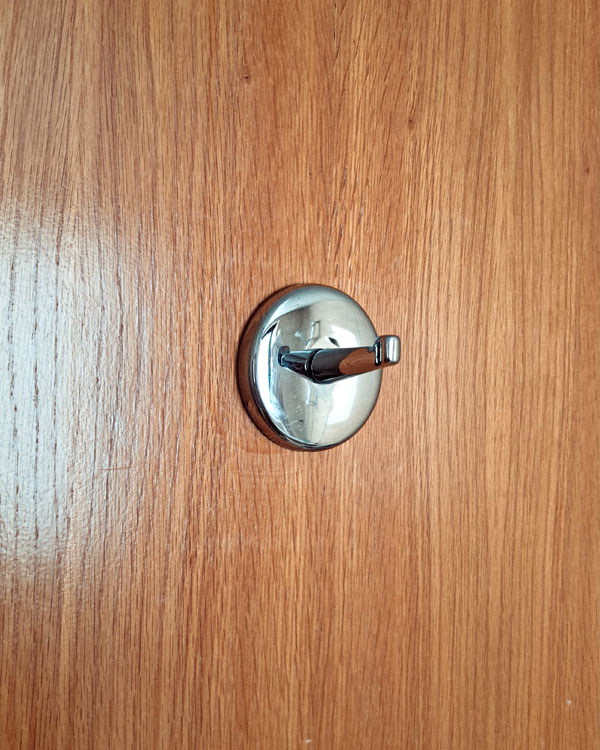 A single hook made of metal, chrome, screwed to a door. Found on a hotel in Porto, Portugal, 2025.