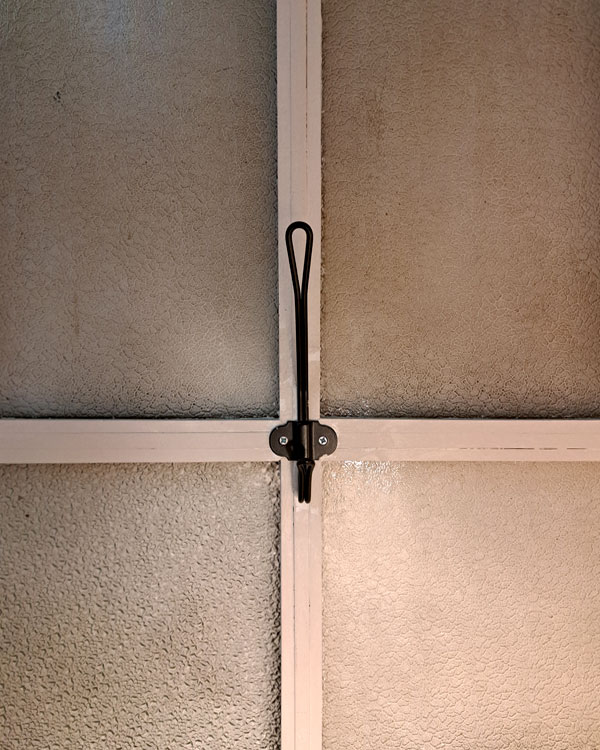 A double hook made of metal, black powder, screwed to a window frame. Found on a store in Porto, Portugal, 2025.