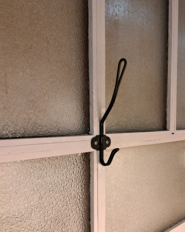 A double hook made of metal, nickel, screwed to a window frame. Found on a store in Porto, Portugal, 2025.