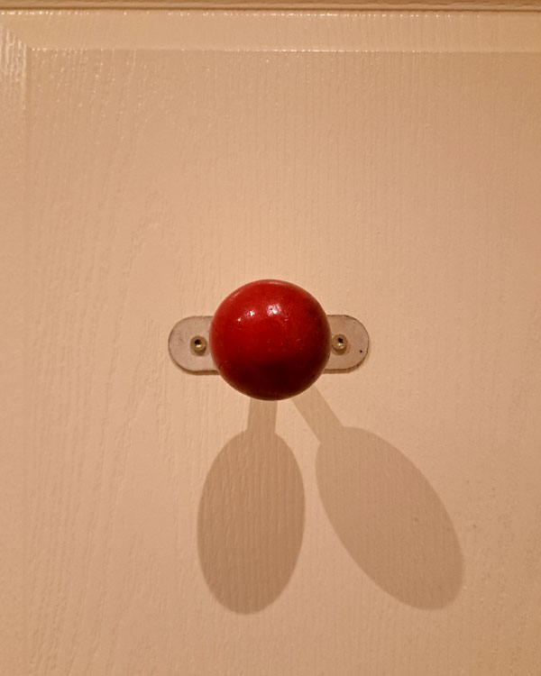 A single hook made of metal and wood, paint, screwed to a door. Found on a hotel in Arles, France, 2025.