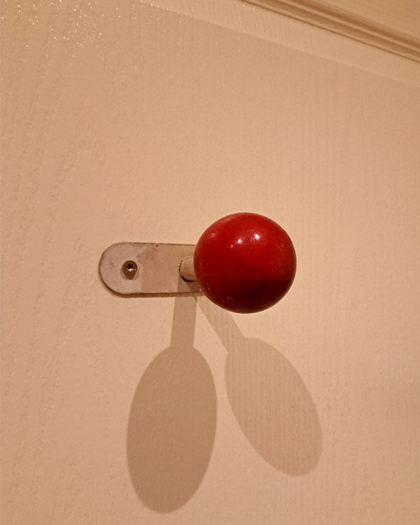 A single hook made of metal and wood, paint, screwed to a wall. Found on a hotel in Arles, France, 2025.