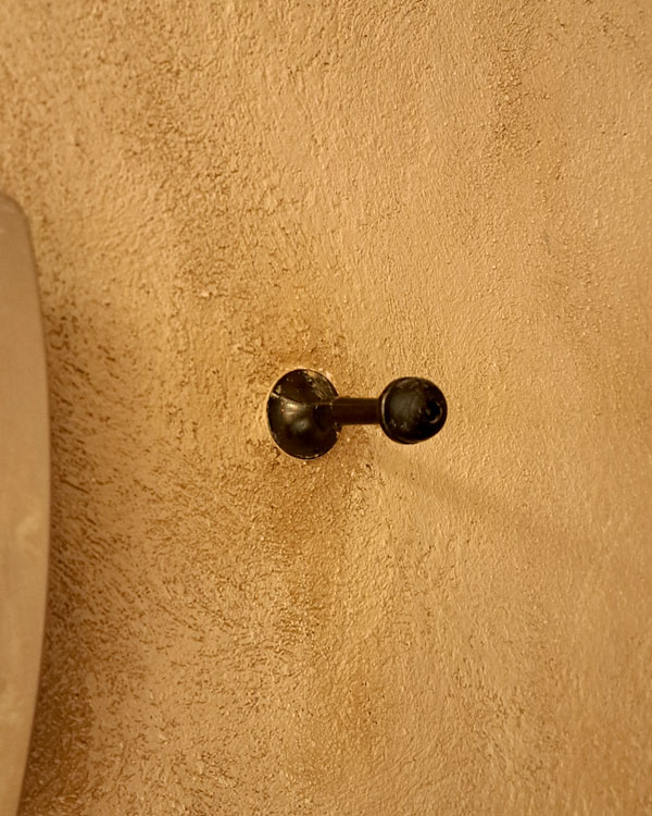 A single hook made of metal and plastic, nickel, screwed to a wall. Found on a restaurant in Mexico City, Mexico, 2026.