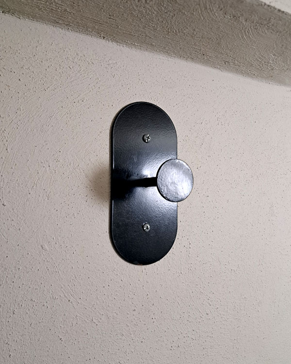 A single hook made of metal, black powder, screwed to a wall. Found on a restaurant in Mexico City, Mexico, 2026.