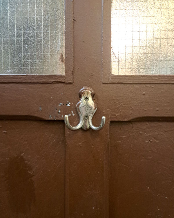 A double hook made of metal, chrome, screwed to a door on a restaurant in Paris, France, 2026.